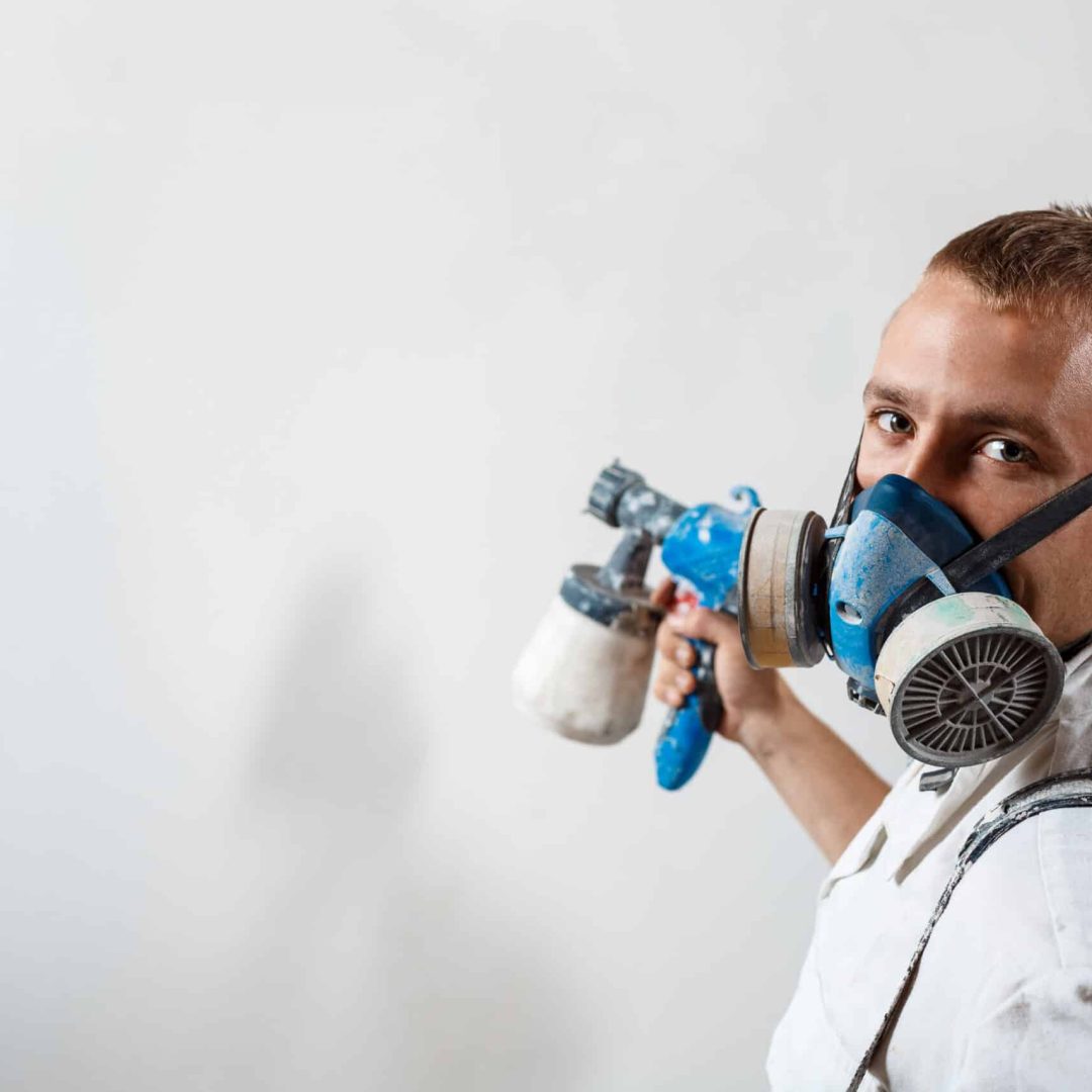 Worker looking at camera, painting wall with spray gun in white color. Copy space.